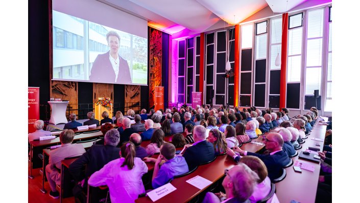 NRW-Wissenschaftsministerin Ina Brandes spricht zu den rund 500 Gästen in der Aula der TH Köln in einer Videobotschaft