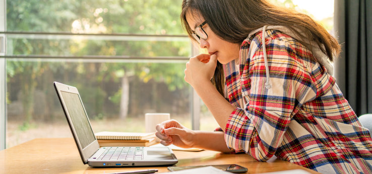 Studentin sitzt an einem Schreibtisch und schaut auf ihr Laptop (Image: adobe stock)
